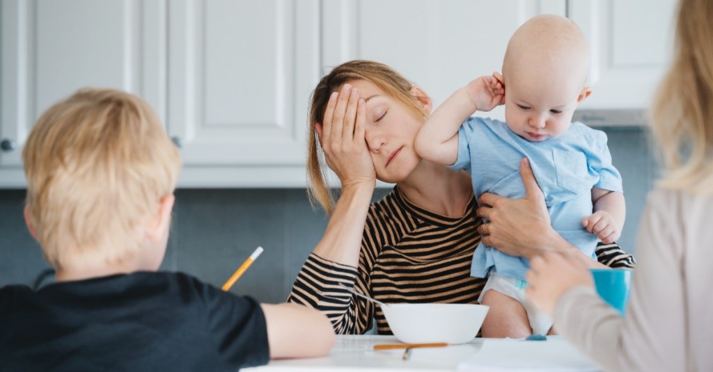 erschöpfte Mutter sitzt am Tisch mit ihren Kindern