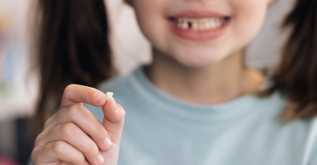 Kleines Mädchen hält einen Milchzahn in der Hand