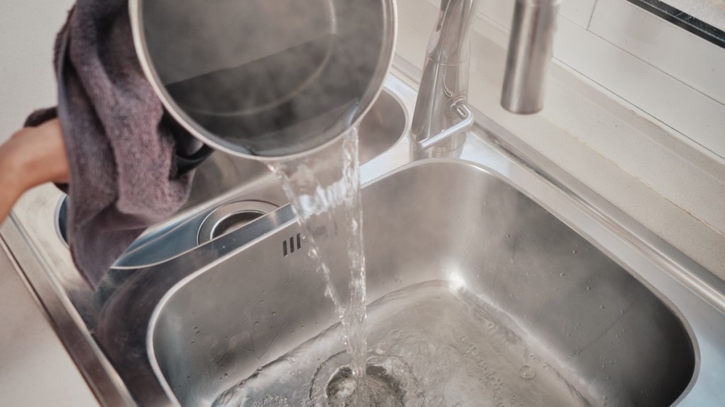 Jemand gießt heißes Wasser in einen Küchenabfluss.