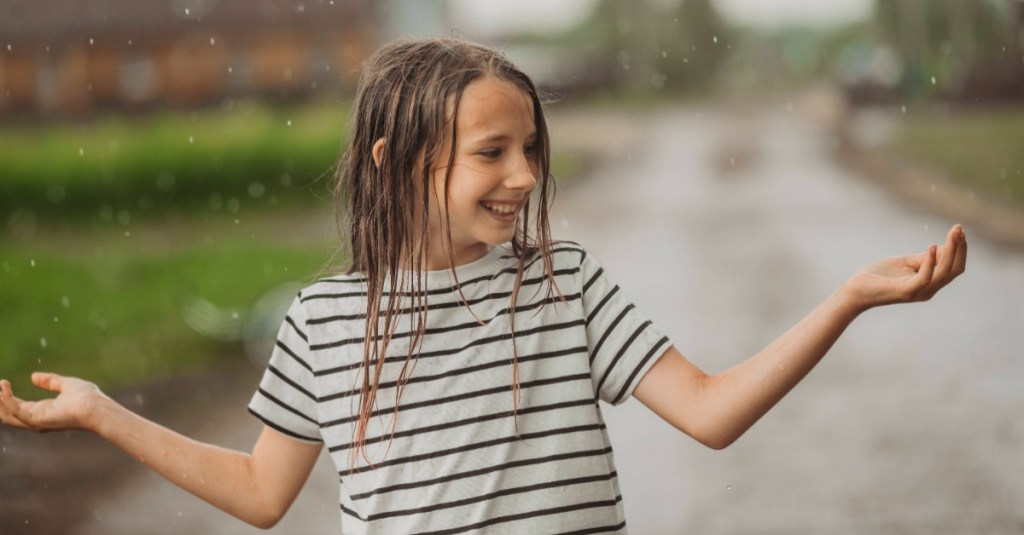 Mädchen spielt im Regen draußen mit nassen Haaren