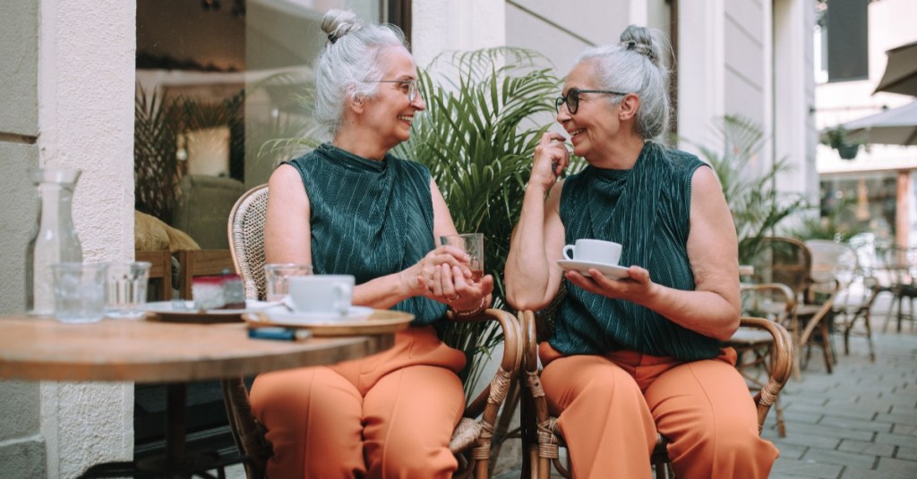 fröhliche Senioren-Zwillinge in gleicher Klediung trinken einen Kaffee 