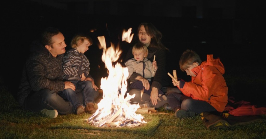 Familie mit drei Kindern sitzt am Lagerfeuer