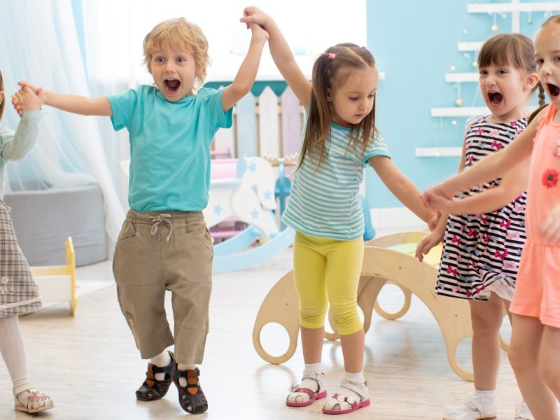 eine Gruppe fröhlicher Kinder tanzt im Kindergarten