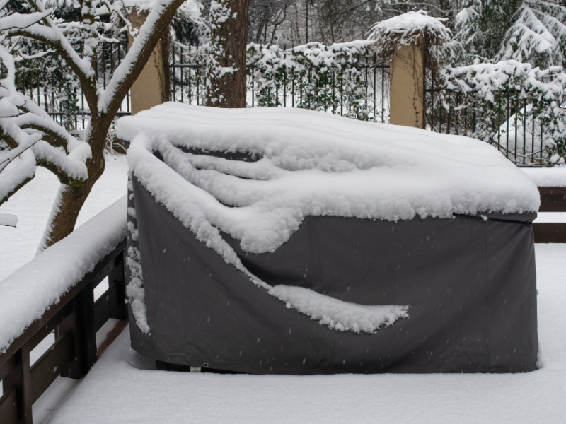 Abgedeckte Gartenmöbel, auf denen Schnee liegt.