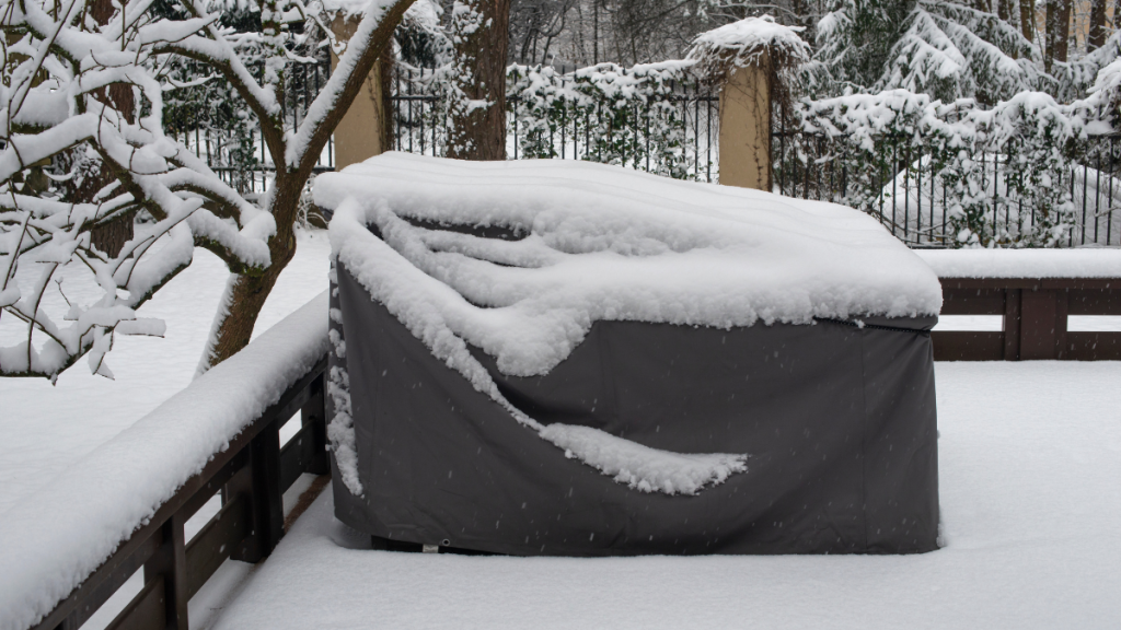 Abgedeckte Gartenmöbel, auf denen Schnee liegt.