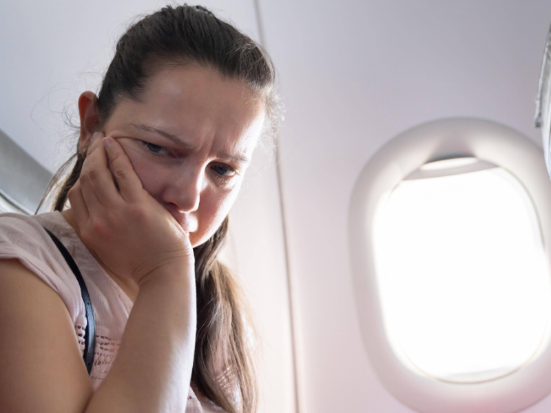 Frau mit Flugangst sitzt im Flugzeug und hat den Kopf auf die Hand gestützt.