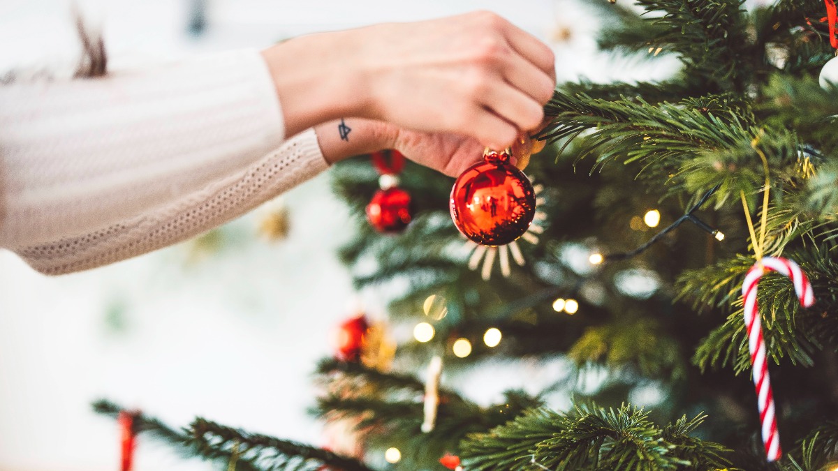 weihnachtlich dekorieren: eine Frau hängt eine Christbaumkugel an den Weihnachtsbaum