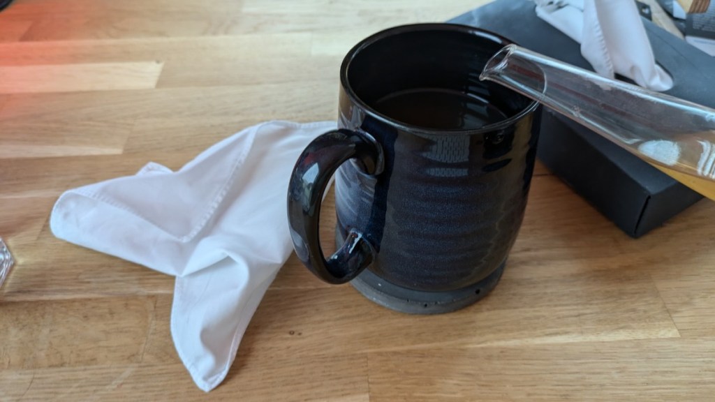 Eine blaue Teetasse, in die Tee eingegossen wird. Daneben liegt ein zerknülltes Taschentuch.