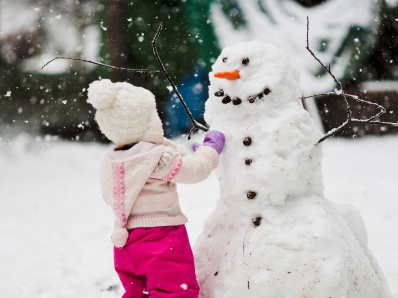 Schneemann bauen: ein kleines MÃ¤dchen steht vor einem Schneemann