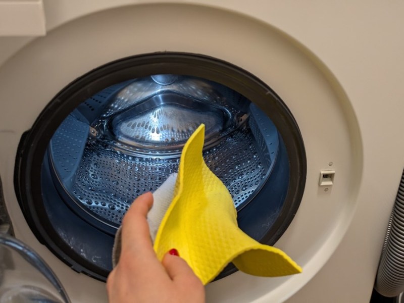 Eine Person steckt einen gelben Putzlappen in die Wäschetrommel einer Waschmaschine.