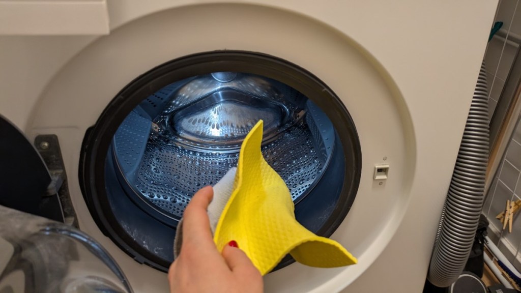 Eine Person steckt einen gelben Putzlappen in die Wäschetrommel einer Waschmaschine.