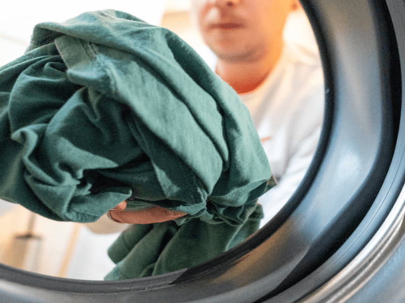 Ein Mann wirft Kleidung in eine Waschmaschine.