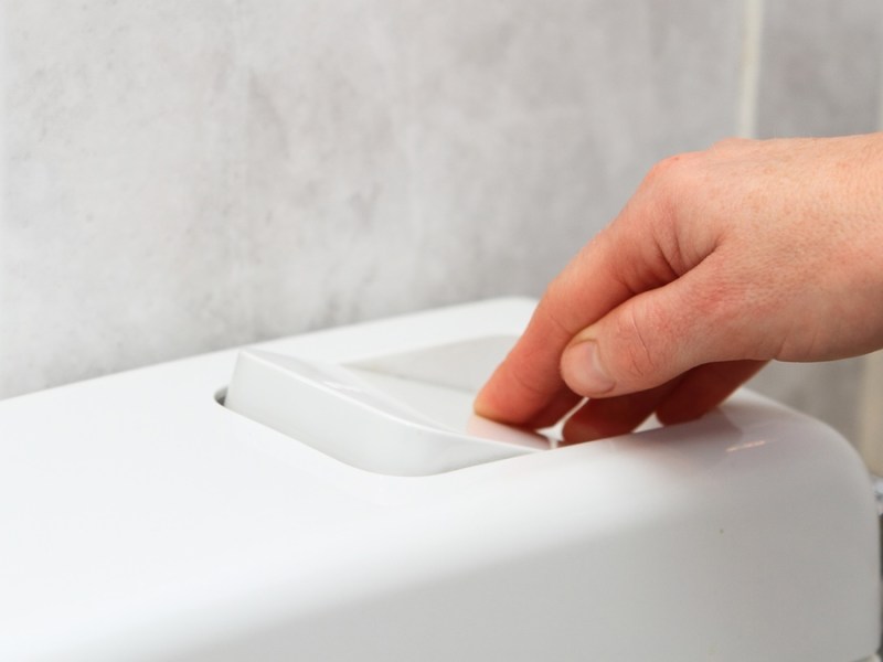 Eine Hand betätigt den Spülknopf an Spülkasten einer Toilette.
