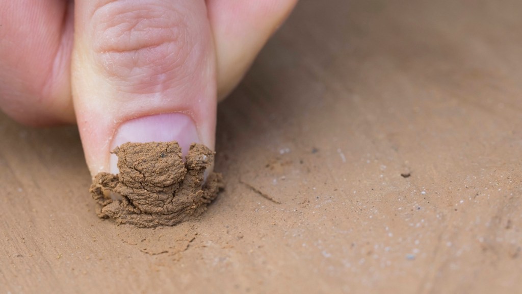 Finger schabt eine Oberfläche aus Lehm ab.