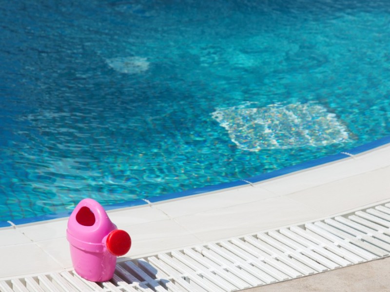eine rosafarbene Kindergießkanne steht an einem Pool